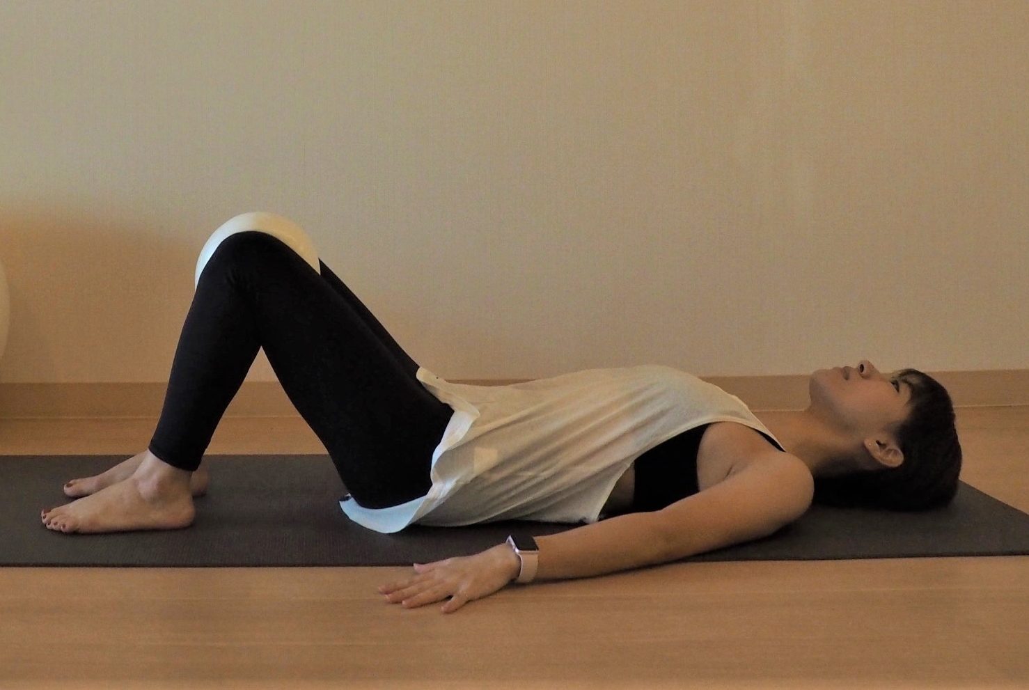 (1) 床に仰向けになりひざを立てたら、ひざとひざの間にクッションを挟む