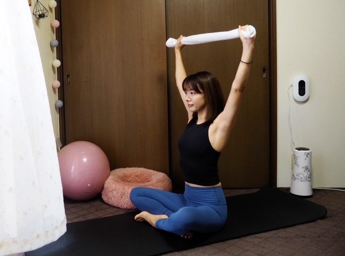 (1) 床や椅子に座り、タオルの両端を手で持ったら腕を頭上に伸ばす。