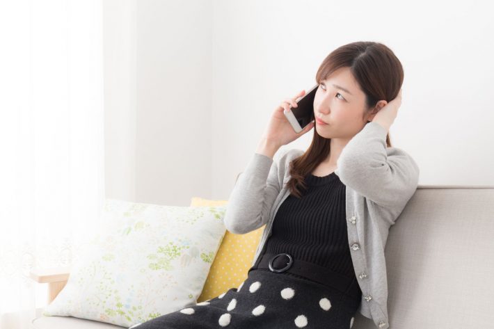 スマホを片手に考える女性