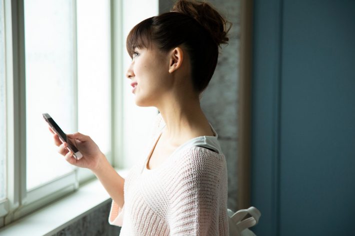 窓辺でスマートフォンを操作する女性