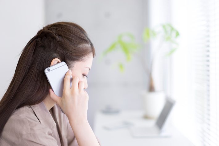 窓際で通話をする若い女性