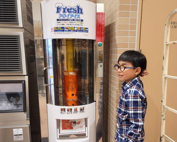 ドライアイスの販売機の前に立つ息子