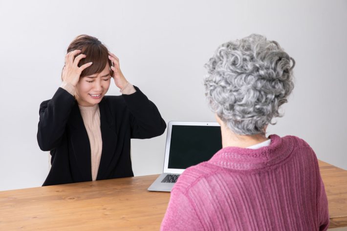 高齢者と話しながら頭を抱える女性