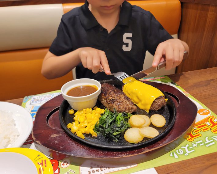 ナイフとフォークを使ってハンバーグを食べる息子