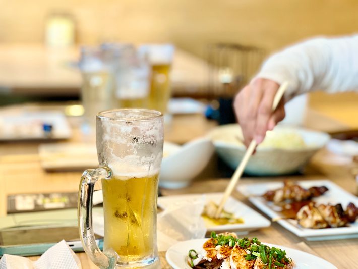 飲みかけのビールグラスと箸を伸ばす手元