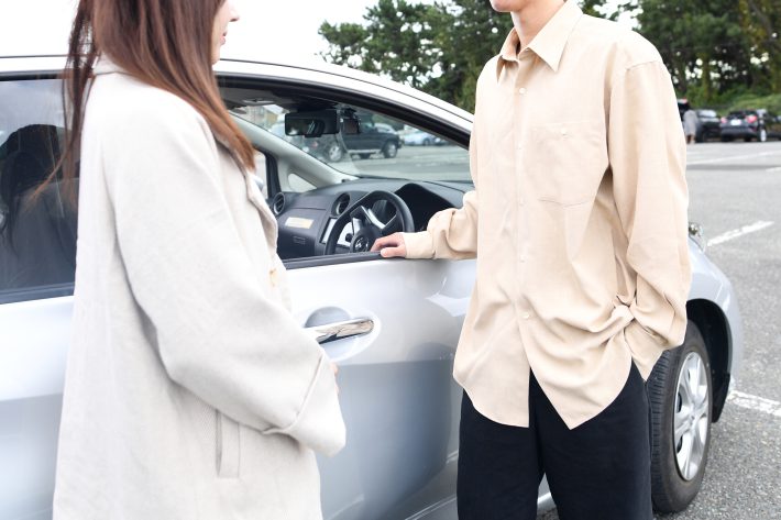 車の前で会話をする男女のアジア人カップル