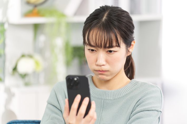 眉間にシワを寄せてスマホを眺める女性