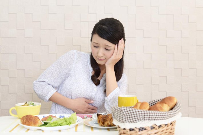 卓上の食べ物を眺めながらお腹をおさえる女性