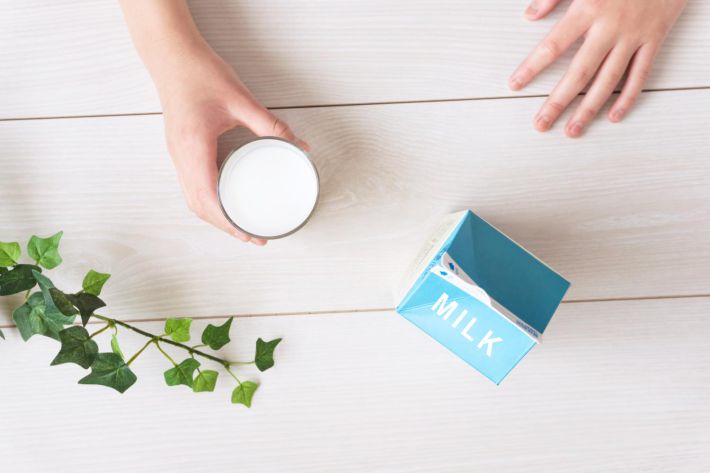 グラスに入った牛乳を飲む人と牛乳パック